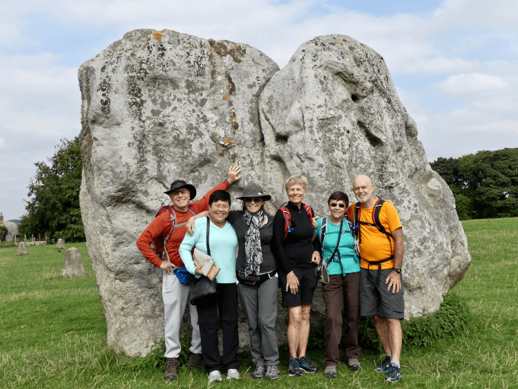 A walking holiday group cluster in their hiking gear in front of a standing stone at Avebury. The rock is so huge it creates a great backdrop for all six of them, and wouldn't be eclipsed even by a larger party.