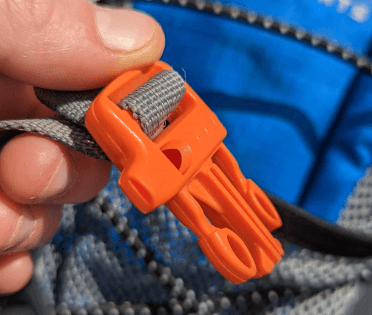An orange whistle built into the buckle of an outdoorsy daypack.